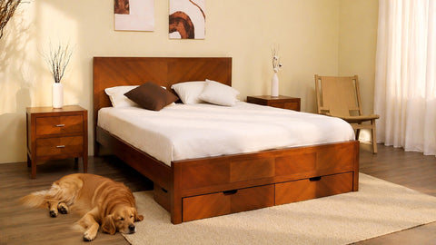 A beautifully detailed frontal photograph of a serene modern bedroom. At the center is a large wooden storage bed with a distinct herringbone-style geometric inlay pattern across the headboard and footboard. The footboard includes two functional storage drawers. The bed is dressed with clean white linens and several white pillows with one dark brown accent pillow. Identical wooden three-drawer nightstands, featuring the same inlay pattern, flank the bed. To the far left, a towering decorative dried branch a
