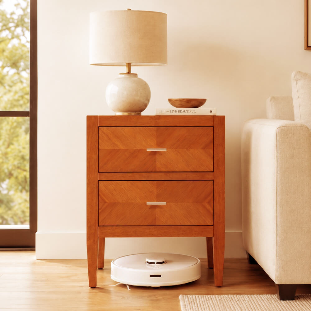 Solid wood 2-drawer nightstand in walnut finish styled with a ceramic table lamp and decorative bowl, robot vacuum underneath

